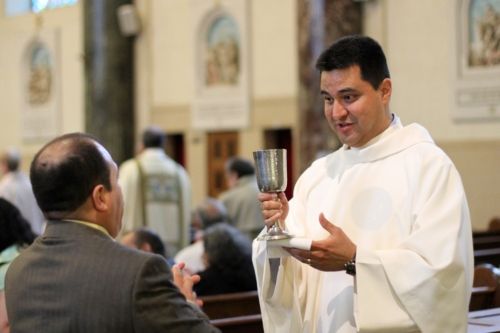 A priest is holding a cup in front of a man.