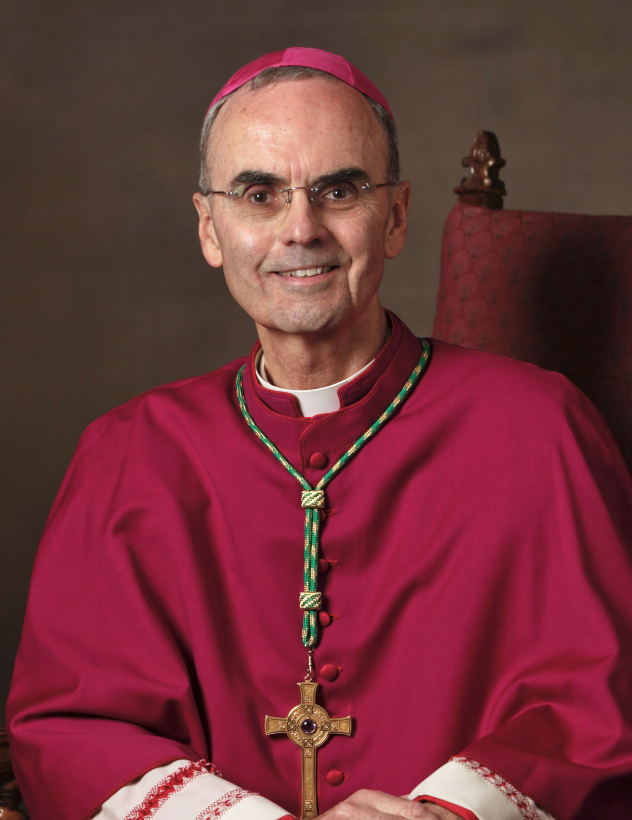 A priest in a red robe sitting in a chair.