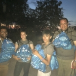 A group of people holding blue backpacks at dusk.
