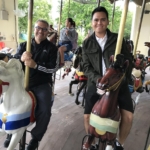 Two men riding horses on a carousel.