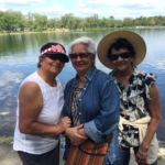 Three women standing next to a body of water.