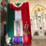 A woman kneeling in front of a mexican flag and a statue of guadalupe.