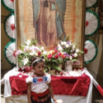 A little girl standing in front of a statue of guadalupe.