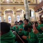 A group of people in green hoodies clapping in a church.