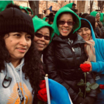 A group of women in green hoodies with roses in their hands.