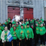 A group of people in green shirts standing in front of a church.