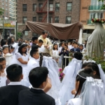 A group of children dressed in white are gathered around a statue of the virgin mary.