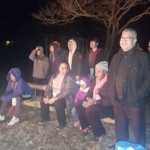A group of people sitting on a bench at night.