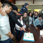 A group of people standing around a birthday cake.