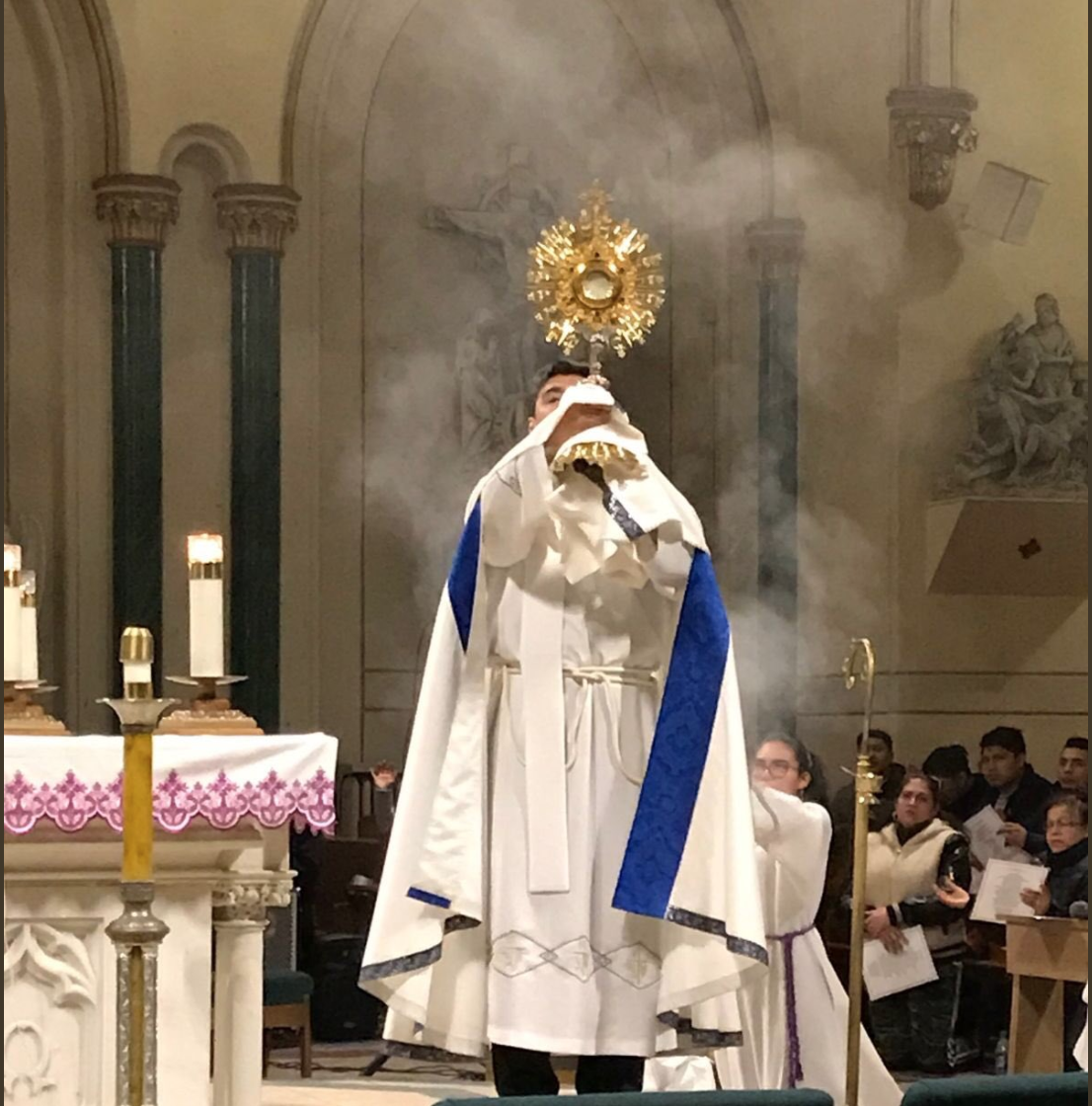 A priest is holding a crucifix in front of smoke.