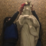 Two people are putting flowers on a statue of the virgin mary.