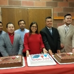 A group of people standing in front of a table with a cake.