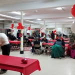 A group of people sitting at tables in a room with red balloons.