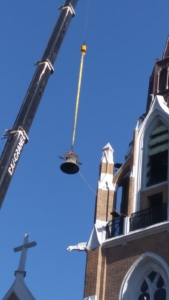 A crane is lifting up the bell from the side of a building.