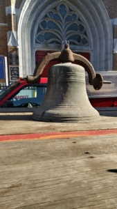 A bell is sitting on the side of the road.