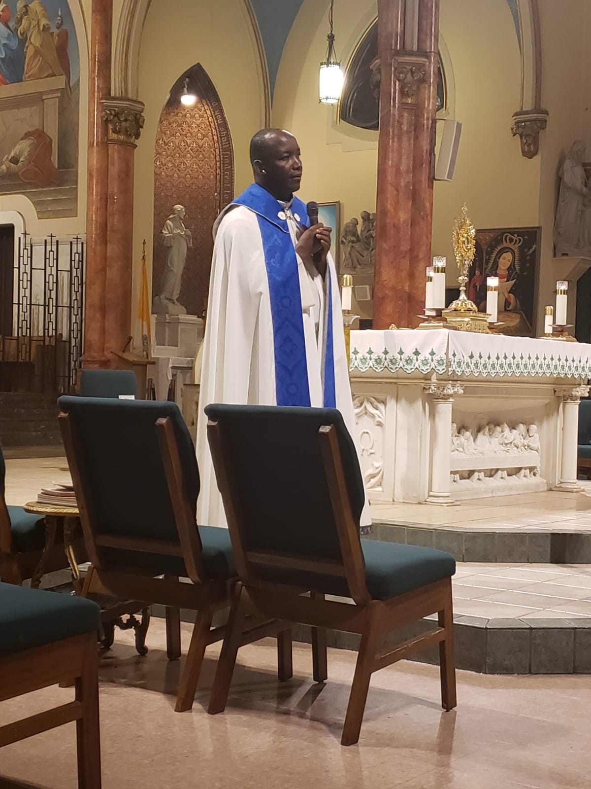 A priest is standing in front of chairs.