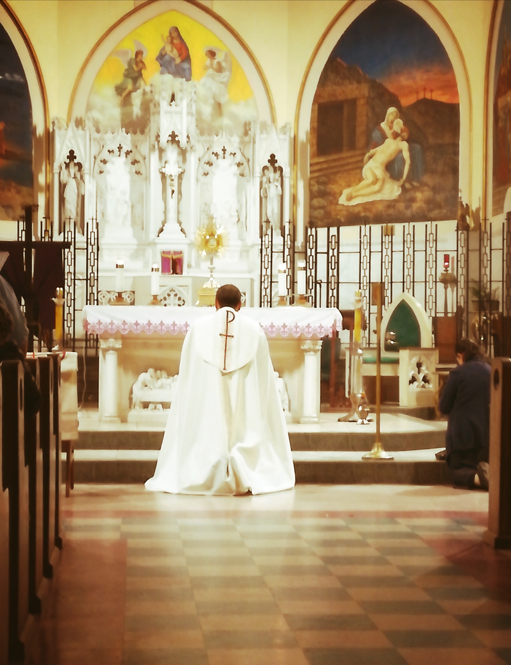 A priest kneeling down in front of the altar.