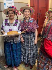 Three women in colorful outfits holding a plate of food.