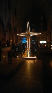 A cross lit up in the middle of an indoor church.