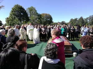 A group of people standing around a coffin.