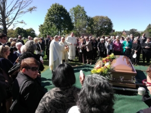 A crowd of people gathered around a casket.