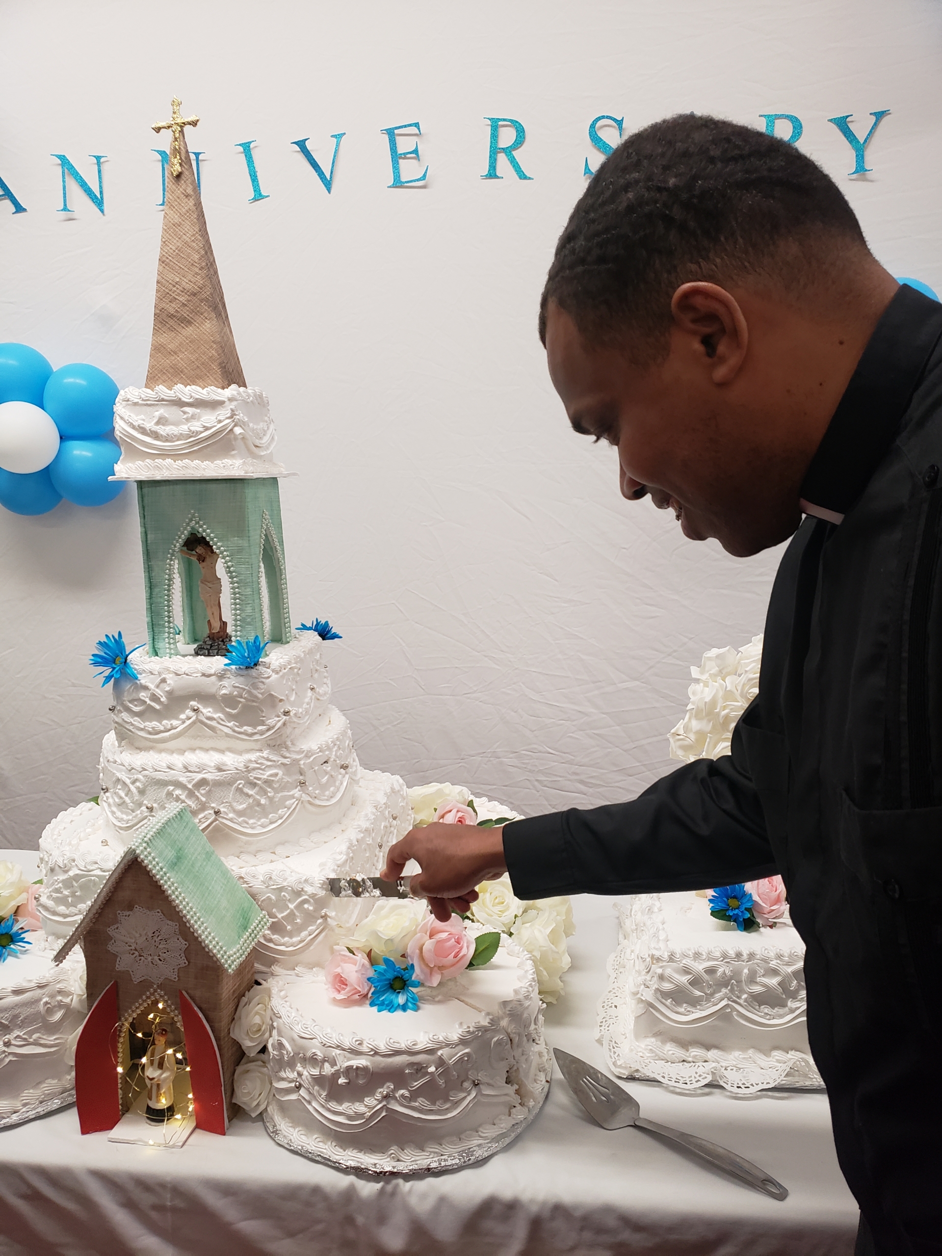 A man cutting a cake with a church on top of it.