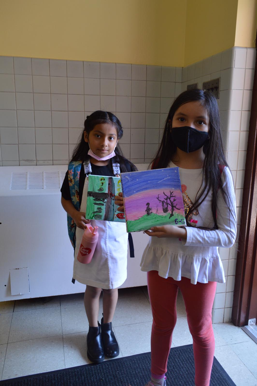 Two girls holding a book in front of a wall.